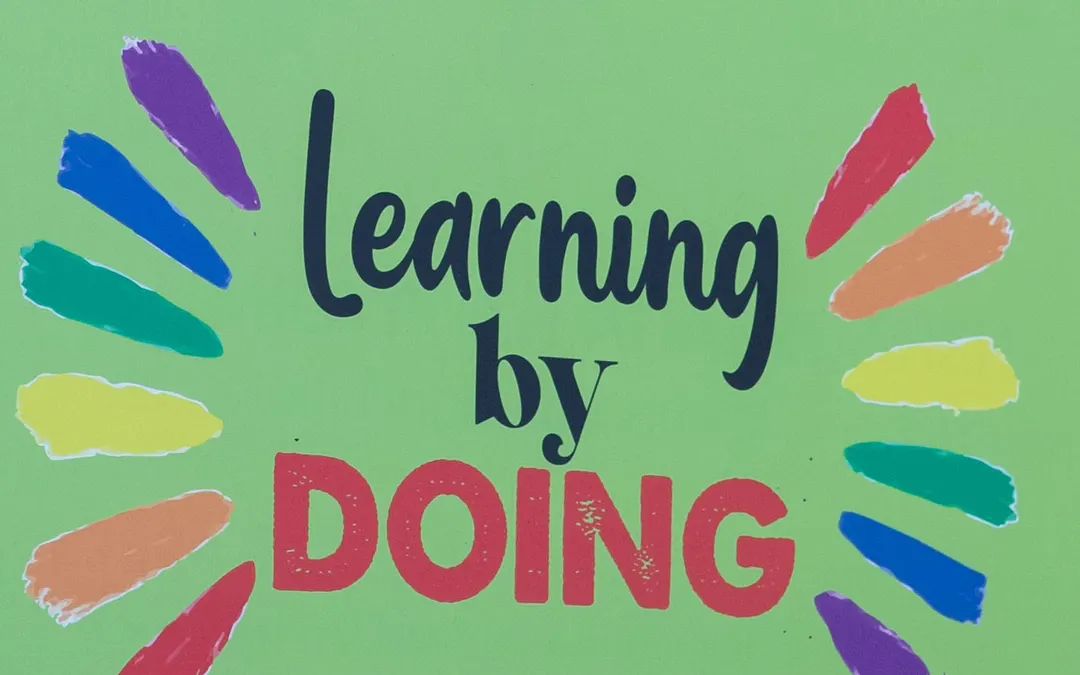 Το σήμα της Ευρωπαιδείας «learning by doing», ζωγραφισμένο σε πράσινο φόντο με χρωματιστές ακτίνες γύρω του.